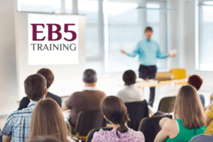 A diverse group of individuals seated in chairs facing a whiteboard displaying the words "EB5 training"