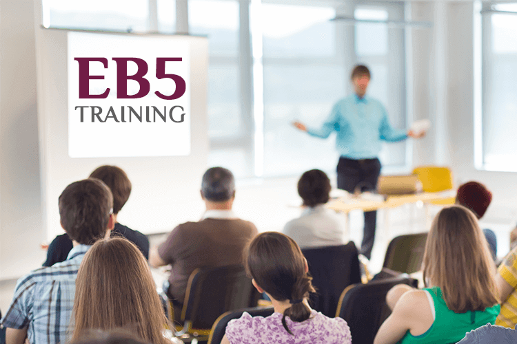 A diverse group of individuals seated in chairs facing a whiteboard displaying the words "EB5 training"
