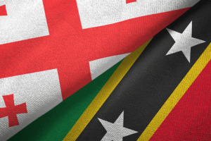 Two flags side by side: one is the flag of St. Kitts, featuring green, red, and black stripes, and the other is the flag of Georgia, with a red background and a white coat of arms