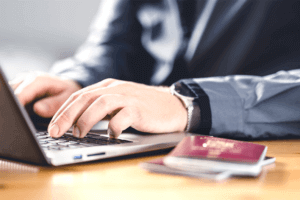 A focused person typing on a laptop beside him a second passport