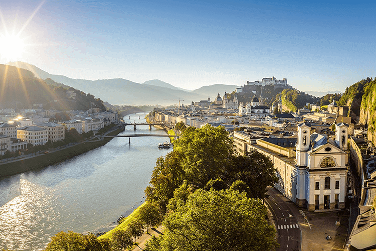 A picturesque cityscape with a river flowing under a bridge, while a majestic castle stands in the background