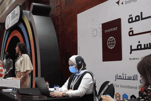 A woman wearing a face mask and scarf sits at a table with a laptop, focused on her work