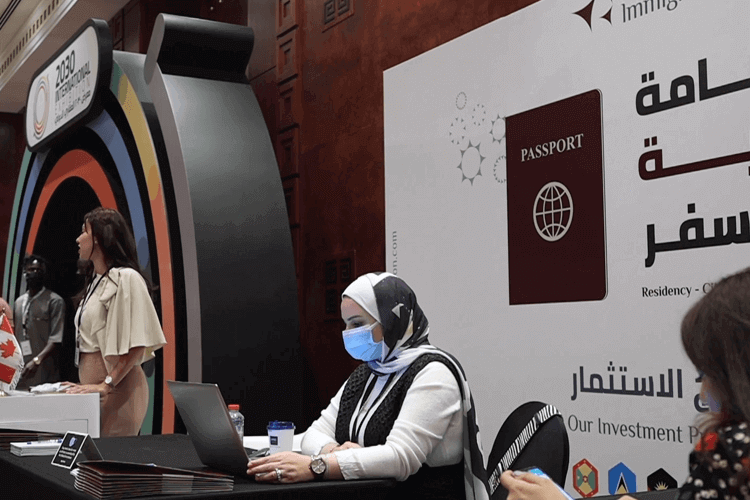 A woman wearing a face mask and scarf sits at a table with a laptop, focused on her work