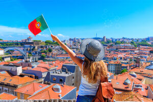 A woman proudly holds a Portuguese flag in front of a bustling city, showcasing her patriotism and love for her country